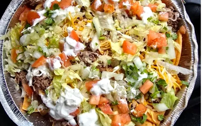 Mike's Nachos loaded with beef, lettuce, tomato, cheese and sour cream in a foil pan