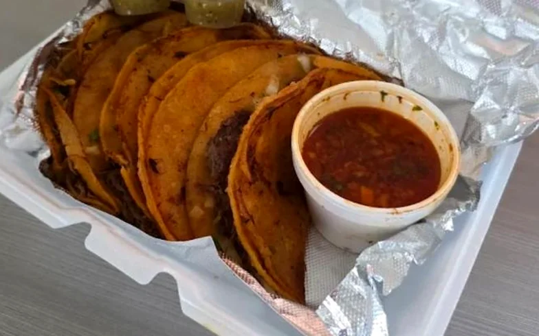 A takeout box of birria tacos with red salsa and two cups of salsa verde